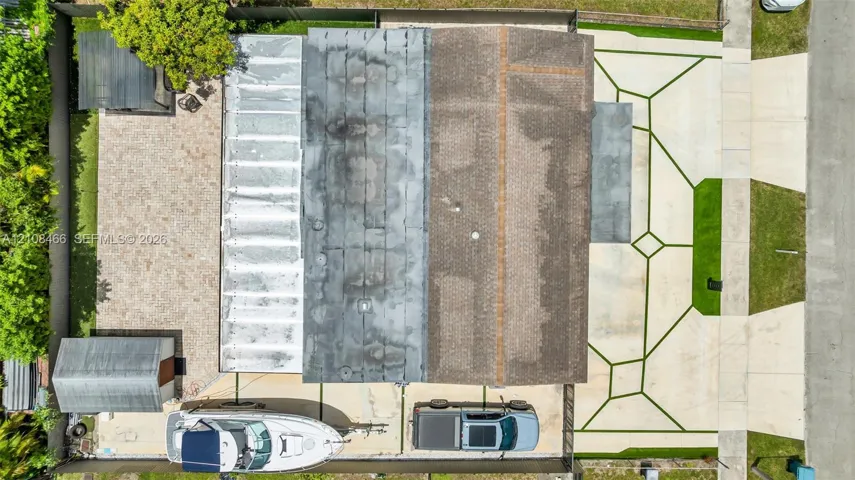 Aerial perspective featuring a multi-section roof, a geometric concrete paved driveway, a gravel backyard area, and a detached storage structure