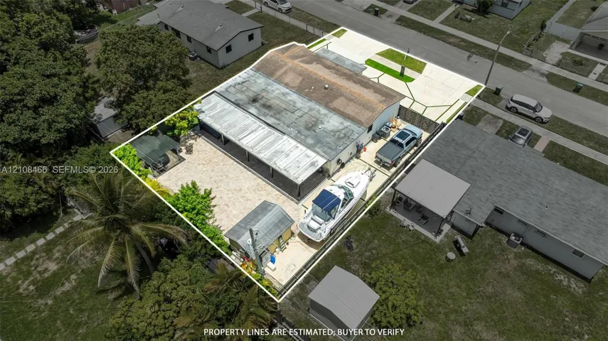 Aerial perspective of residential property featuring a concrete driveway, gated gravel parking area, metal-covered patio, and a detached storage structure