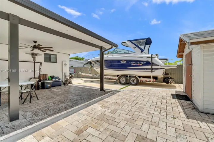 Covered outdoor living space featuring a dark-toned support structure and ceiling fan, paver-finished patio, and an external storage shed