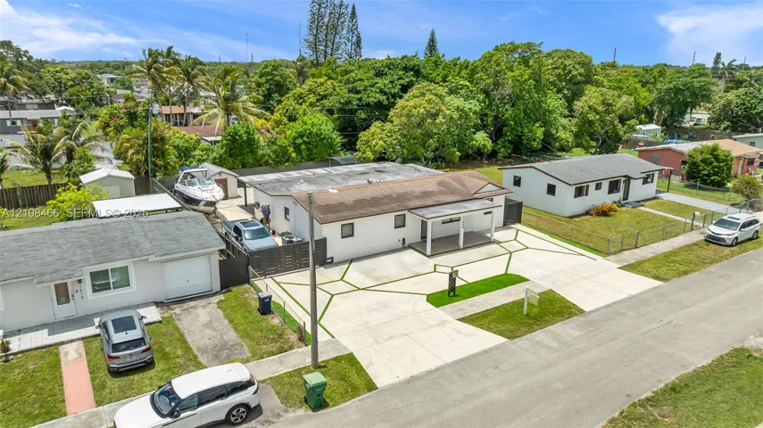 Single-story residence featuring a concrete exterior, covered front porch, custom geometric-pattern concrete driveway with inset grass turf, and enclosed outdoor storage areas