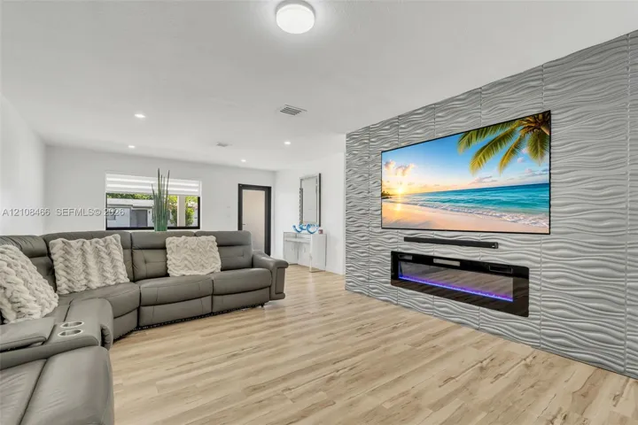 Living area featuring light-toned wood-finish flooring, a textured 3D accent wall, and a built-in linear electric fireplace