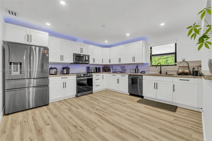 Kitchen featuring white shaker cabinetry, stainless steel appliances, stone-finish countertops, recessed lighting, and wood-finish flooring