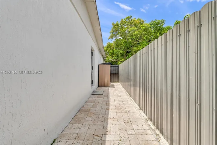 Exterior side yard featuring light-colored stone pavers and a corrugated metal privacy fence