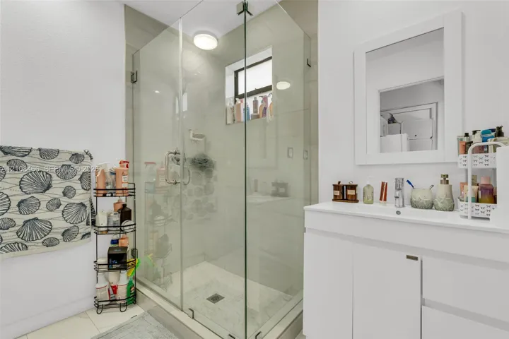 Frameless glass shower enclosure with tiled walls, white vanity featuring an integrated sink, and a wall-mounted framed mirror