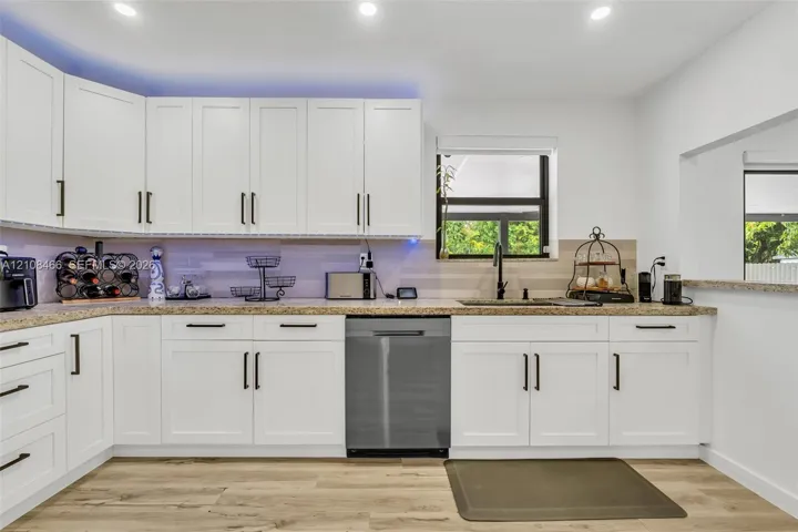 Kitchen featuring white shaker-style cabinetry, stone-finish countertops, stainless steel dishwasher, wood-finish flooring, and recessed ceiling lighting