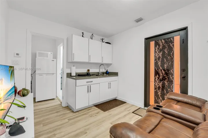 Kitchenette featuring white cabinetry, a sink with a metal faucet, solid-surface countertops, and wood-finish flooring, accented by an exterior door with a patterned glass insert
