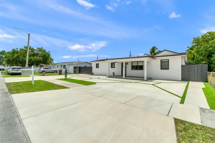 Single-story residence featuring a smooth stucco exterior, a geometric concrete driveway with turf-accented inlay, a covered front entryway, and privacy-focused perimeter fencing