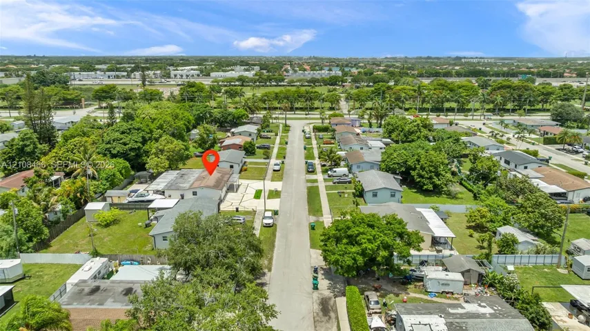 Aerial perspective of a residential property featuring a paved driveway, a spacious backyard, and mature surrounding landscaping