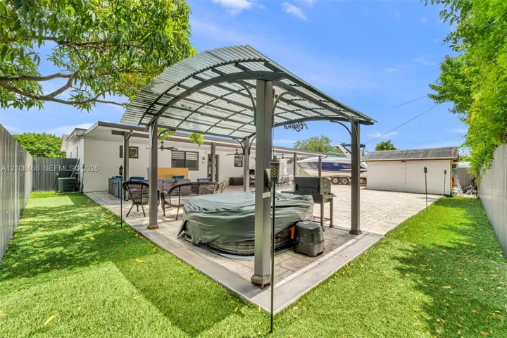 Backyard featuring a paved patio, a metal-framed pergola with a corrugated roof, and a detached storage structure