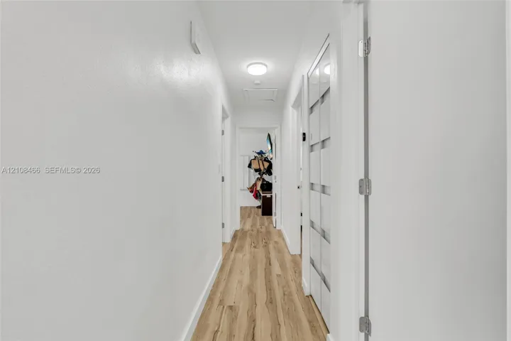 Hallway featuring wood-finish flooring, white walls, flush-mount ceiling lighting, and a multi-panel door with glass inserts