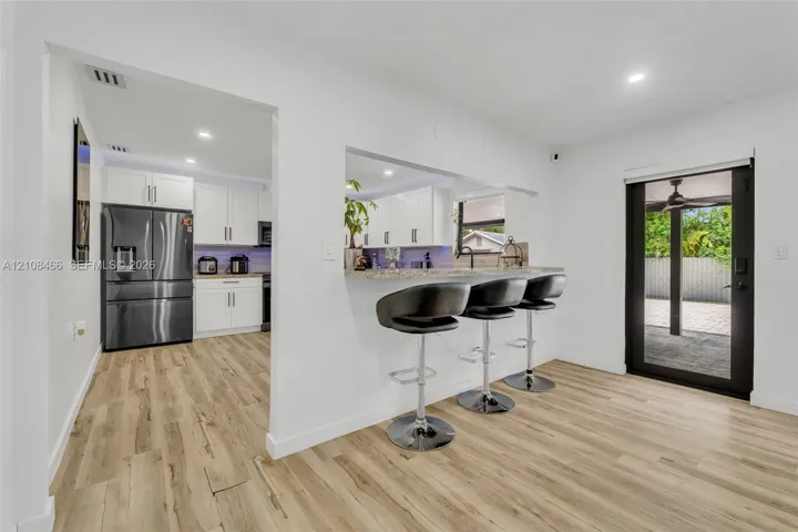 Kitchen featuring white shaker cabinetry, stone-finish countertops, stainless steel appliances, wood-finish flooring, and a breakfast bar cutout