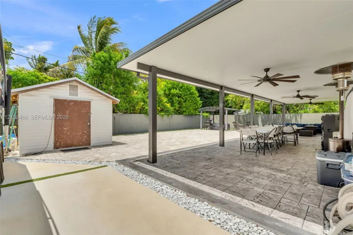 Covered outdoor patio with stamped concrete flooring and ceiling-mounted fans, featuring a detached storage structure and perimeter fencing