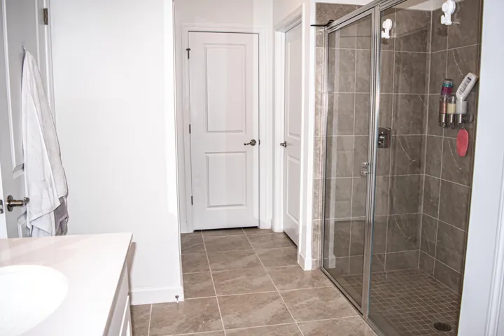 Bathroom featuring a walk-in shower with glass enclosure, neutral tile flooring, tiled shower walls, and a vanity with a solid-surface countertop
