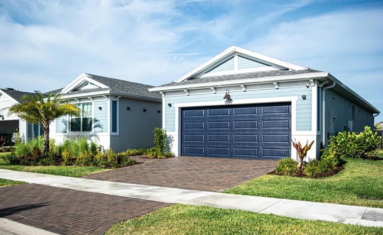 Exterior featuring lap siding, asphalt shingle roof with gable accents, carriage-style garage door, and paver driveway