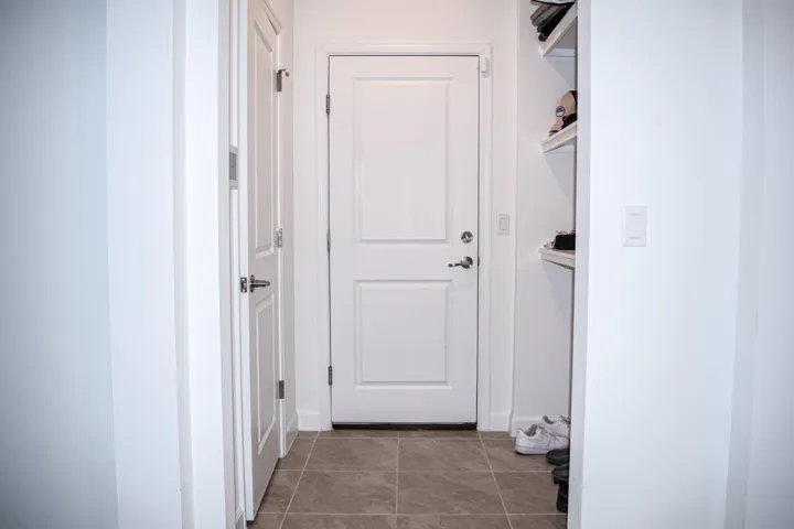 Neutral-toned stone-finish tile flooring featuring a white paneled door, integrated wall shelving, and a secondary interior door with metallic hardware