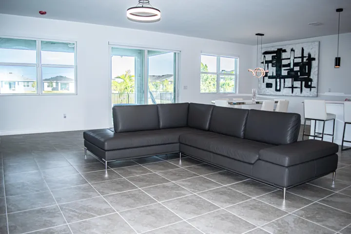Open-concept interior featuring large-format ceramic tile flooring, multiple windows, sliding glass door, and modern multi-light fixtures