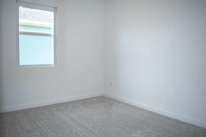 Neutral interior room featuring neutral-toned carpeting and a window with a fitted roller shade
