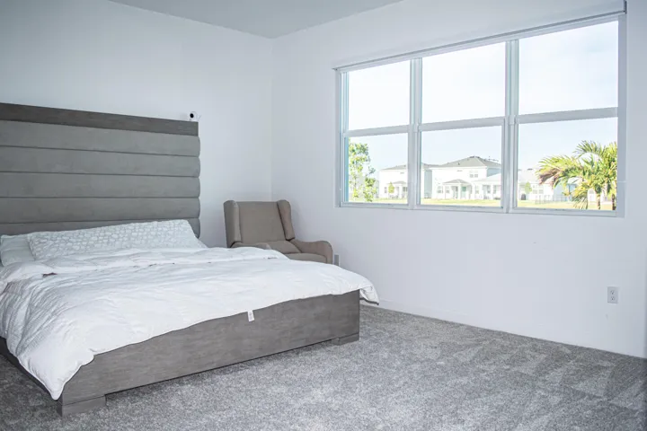Neutral-toned carpet flooring, oversized horizontal window with a retractable roller shade, and smooth white wall finishes