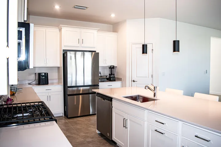 Kitchen featuring white shaker-style cabinetry, a quartz-topped center island with an integrated sink, stainless steel appliances, pendant lighting, and tile flooring