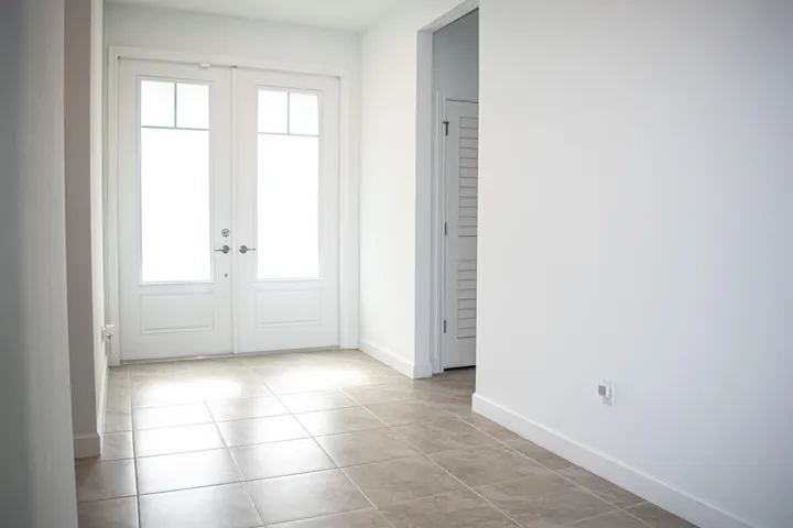 Entryway featuring double glass-paneled doors, neutral tile flooring, and white interior doors with louvered accents
