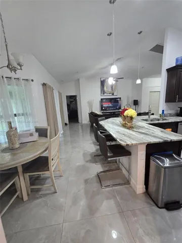 Open-concept area featuring large-format polished tile flooring, vaulted ceilings, and a kitchen island with stone-patterned countertop