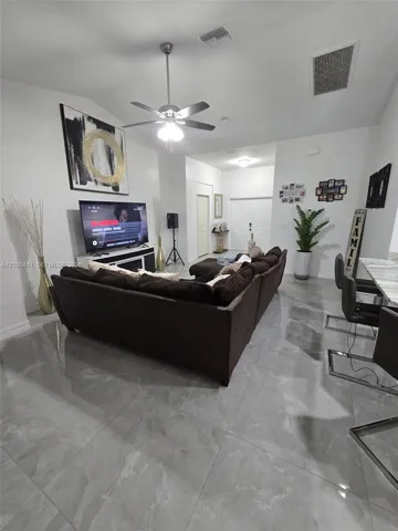 High-ceiling living area featuring large-format polished tile flooring, a brushed nickel ceiling fan with integrated lighting, and neutral wall tones