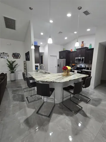 Kitchen featuring dark-finish cabinetry, stone countertops, a multi-seat island with an integrated stainless steel sink, tile flooring, and recessed ceiling lighting