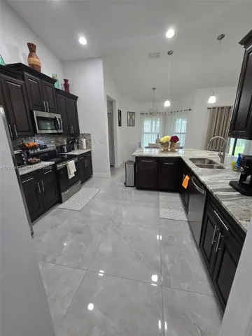 Kitchen featuring dark wood cabinetry, large-format polished tile flooring, stone-finish countertops, stainless steel appliances, and pendant lighting