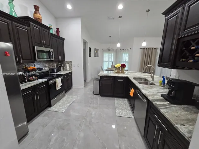 Kitchen featuring dark wood cabinetry, integrated wine storage, natural stone countertops, tile flooring, and stainless steel appliances