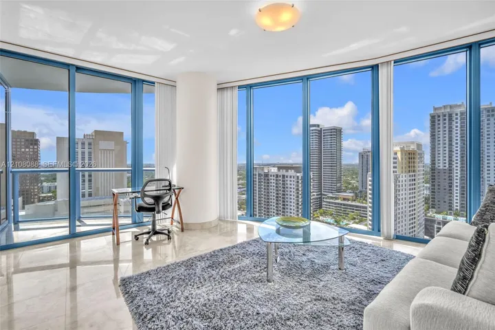 Floor-to-ceiling windows featuring panoramic urban scenery, polished stone flooring, and a glass balcony railing