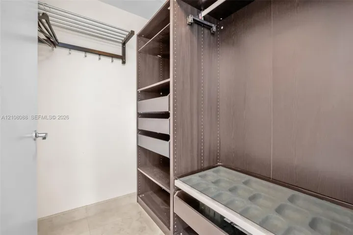 Walk-in closet featuring custom wood-finish cabinetry, built-in shelving, integrated pull-out drawers, a glass-topped accessory organizer, and wall-mounted garment racks