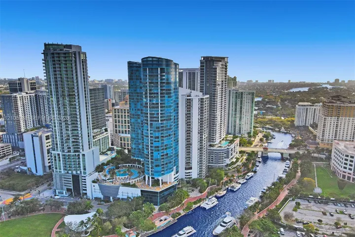 Aerial perspective of high-rise urban towers featuring glass-facade architecture, a multi-level swimming pool terrace, and water-front placement along a canal
