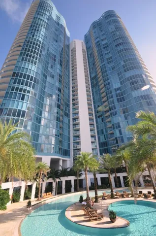 High-rise glass facade featuring curvilinear architecture, private balconies, and a multi-level swimming pool with hardscaped patio