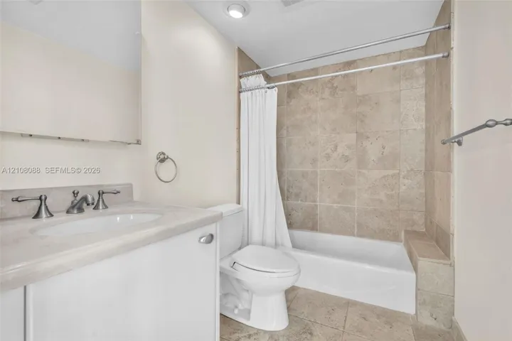 Bathroom featuring natural stone tile tub surround and flooring, vanity with stone countertop, recessed lighting, and metallic hardware