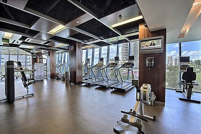 Fitness facility featuring floor-to-ceiling windows, wood-paneled structural columns, grid-patterned recessed ceiling panels, and neutral resilient flooring