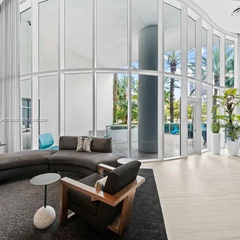 Curved floor-to-ceiling glass wall, light-toned stone tile flooring, and integrated structural column