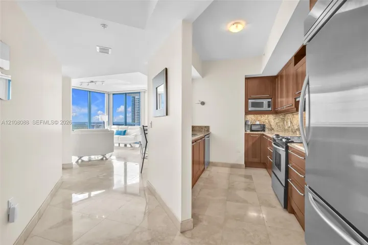 Entry and kitchen featuring wood cabinetry, stone countertops, stone flooring, and stainless steel appliances, with floor-to-ceiling windows
