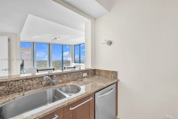 Kitchen featuring stone countertops, stainless steel dual-basin sink, high-arc faucet, built-in dishwasher, and wood cabinetry