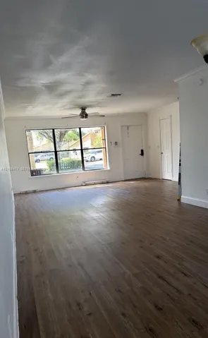 Open-concept interior featuring wood-finish flooring, a large picture window, a ceiling fan, and crown molding
