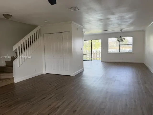 Wood-finish flooring, staircase with white railings, sliding glass door, crown molding, and multi-light chandelier