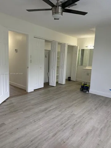 Room featuring wood-finish flooring, a ceiling fan with integrated lighting, dual bi-fold closet doors with built-in shelving, and an attached vanity with a mirror and multi-bulb light fixture