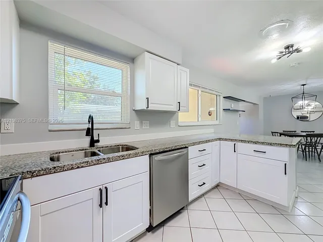Kitchen featuring white shaker-style cabinetry, stone-finish countertops, stainless steel dishwasher, double-basin undermount sink with matte black faucet, and ceramic tile flooring
