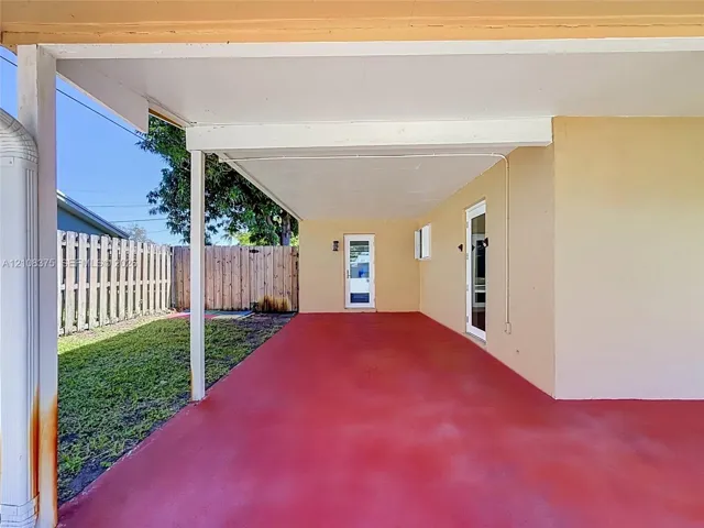 Covered exterior patio with painted concrete flooring, two glass-panel entry doors, and a wood-slat privacy fence