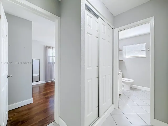 Hallway featuring white dual-panel sliding closet doors, wood-finish flooring, and porcelain tile flooring in the entryways