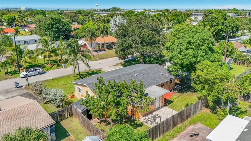 Aerial perspective featuring a single-story residence with a shingled gable roof, exterior patio, wood-style privacy fencing, and mature landscaping