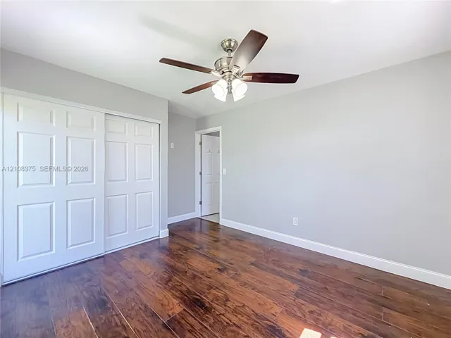 Room featuring wood-finish flooring, a brushed-nickel ceiling fan with a three-light fixture, and a sliding-door closet with white six-panel doors