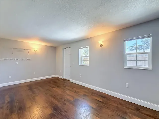 Interior space featuring wood-finish flooring, neutral wall tones, dual wall-mounted light fixtures, multi-pane windows, and a panel door