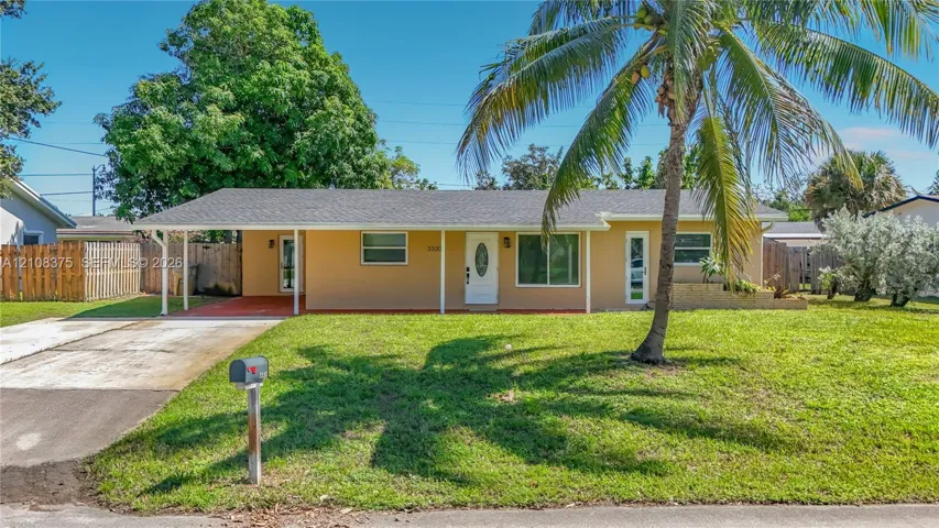 Single-story exterior featuring a concrete driveway, attached carport, manicured lawn, and mature palm tree