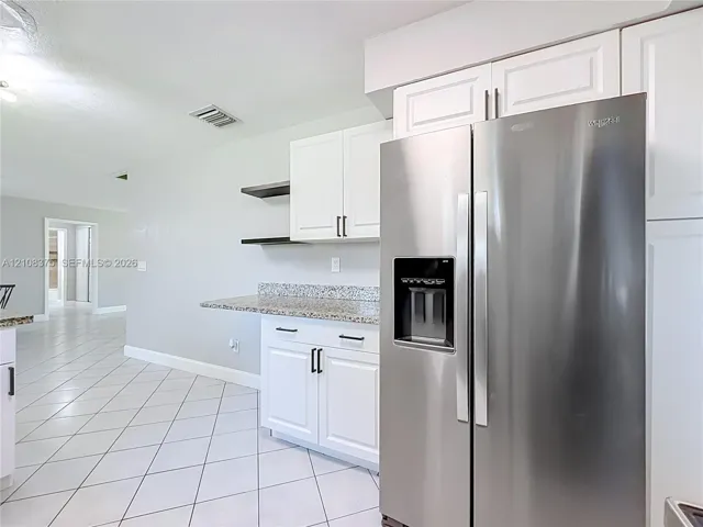 Kitchen featuring white shaker-style cabinetry, stainless steel side-by-side refrigerator, stone-composite countertops, open shelving, and neutral ceramic tile flooring