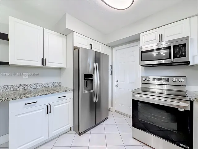 Kitchen featuring white shaker-style cabinetry, stone countertops, stainless steel appliances, and ceramic tile flooring